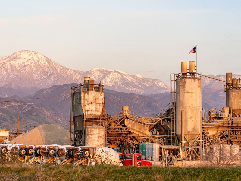 Cement plant with silos, inclined conveyors and material stockpiles at sunset