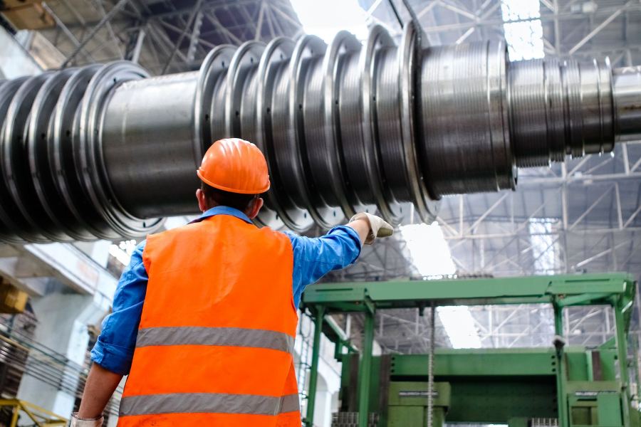 Maintenance engineer in hi-vis and hard hat inspecting a large industrial pulley shaft in a workshop